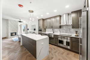 Kitchen with appliances with stainless steel finishes, sink, hanging light fixtures, a center island, and wall chimney range hood