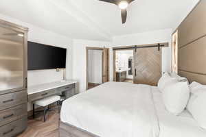 Bedroom featuring ceiling fan, ensuite bathroom, a barn door, and light parquet floors