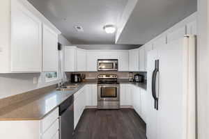 Kitchen with appliances with stainless steel finishes, dark hardwood / wood-style floors, sink, white cabinets, and a textured ceiling