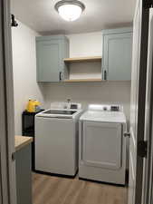 Laundry room with washer and dryer, cabinets, a textured ceiling, and light wood-type flooring