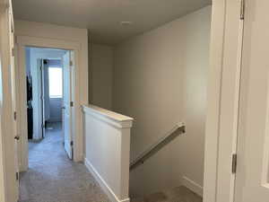 Hallway with a textured ceiling and light colored carpet