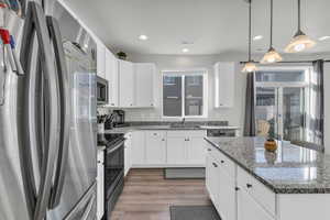 Kitchen with stainless steel appliances, white cabinetry, and hanging light fixtures