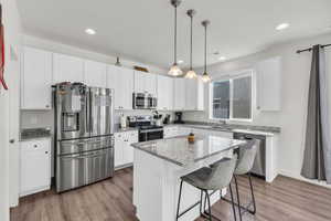 Kitchen with white cabinetry, stainless steel appliances, a kitchen island, and pendant lighting