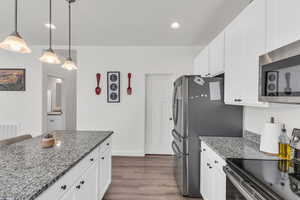 Kitchen featuring white cabinetry, decorative light fixtures, and light stone countertops