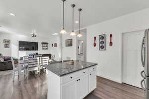 Kitchen featuring pendant lighting, stainless steel refrigerator, white cabinetry, a kitchen island, and dark stone counters