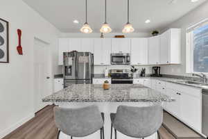 Kitchen with pendant lighting, sink, white cabinetry, stainless steel appliances, and a center island