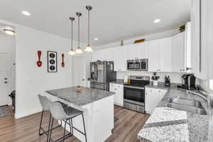 Kitchen with sink, light hardwood / wood-style flooring, a kitchen island, stainless steel appliances, and white cabinets