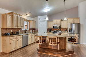 Kitchen with sink, appliances with stainless steel finishes, hanging light fixtures, a kitchen island, and light wood-type flooring