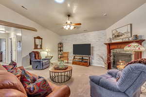 Carpeted living room featuring a tiled fireplace, lofted ceiling, and ceiling fan