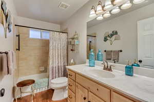 Full bathroom with vanity, hardwood / wood-style floors, shower / bathtub combination with curtain, and toilet