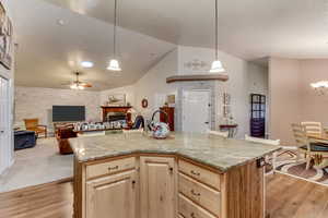 Kitchen featuring light stone countertops, a kitchen island with sink, hanging light fixtures, and light wood-type flooring