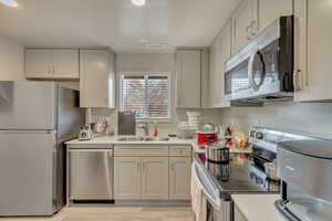 Kitchen with appliances with stainless steel finishes, gray cabinetry, light hardwood / wood-style flooring, and sink