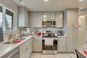 Kitchen featuring stainless steel appliances, gray cabinetry, light wood-type flooring, light stone countertops, and sink