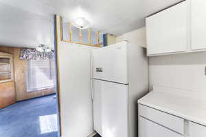 Kitchen featuring a textured ceiling, wooden walls, white cabinets, light colored carpet, and white refrigerator