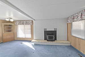 Unfurnished living room featuring wood walls, carpet flooring, and beam ceiling