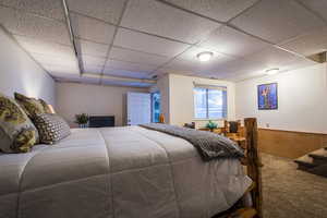 Carpeted bedroom featuring a drop ceiling and wooden walls