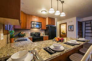 Kitchen featuring tasteful backsplash, black appliances, sink, light stone counters, and kitchen peninsula