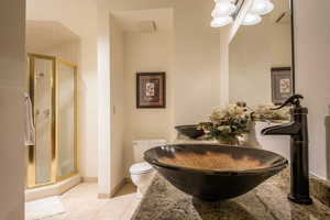 Bathroom featuring tile patterned floors, toilet, an enclosed shower, and dual sinks