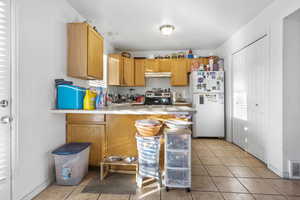 Kitchen featuring white refrigerator, electric stove, light tile patterned floors, and kitchen peninsula