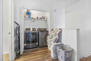 Clothes washing area with hardwood / wood-style flooring and washer and dryer