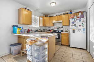 Kitchen with stainless steel range with electric stovetop, light tile patterned floors, kitchen peninsula, and white fridge