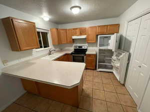 Kitchen with sink, stainless steel electric range oven, a textured ceiling, light tile patterned floors, and kitchen peninsula