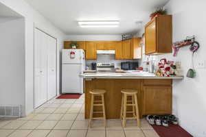 Kitchen featuring a kitchen bar, white refrigerator, light tile patterned floors, electric range, and kitchen peninsula