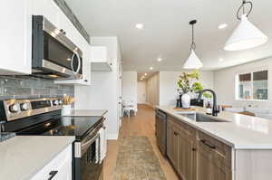 Kitchen featuring white cabinetry, sink, pendant lighting, and appliances with stainless steel finishes