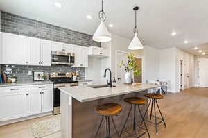 Kitchen featuring stainless steel appliances, sink, decorative light fixtures, and an island with sink