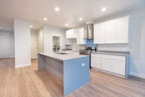 Kitchen with sink, light waterproof luxury vinyl plank flooring, wall chimney range hood, elegant quartz waterfall counter tops, and white cabinets