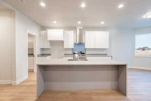 Kitchen featuring sink, white cabinetry, elegant quartz waterfall counter tops, featuring light waterproof luxury vinyl plank flooring, and wall chimney exhaust hood