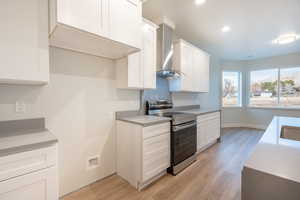 Kitchen with white cabinetry, sink, stainless steel range with electric cooktop, light waterproof luxury vinyl plank flooring, and wall chimney range hood