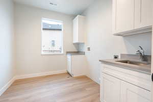 Clothes washing area featuring hookup for a washing machine, sink, hookup for an electric dryer, and light waterproof luxury vinyl plank flooring