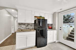 Kitchen with black refrigerator, sink, tasteful backsplash, and white cabinets