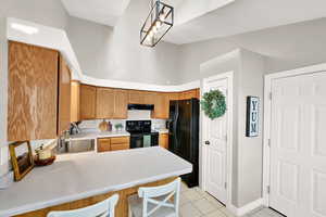 Kitchen featuring light tile patterned flooring, sink, kitchen peninsula, pendant lighting, and black appliances