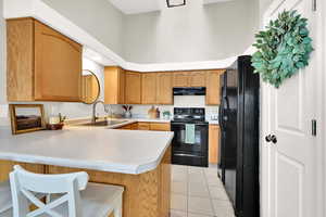 Kitchen featuring sink, a high ceiling, black appliances, light tile patterned flooring, and kitchen peninsula