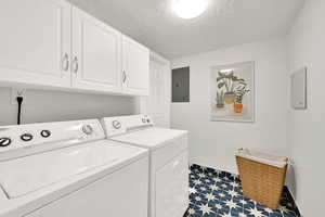 Clothes washing area featuring cabinets, washing machine and clothes dryer, electric panel, and a textured ceiling