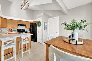 Kitchen with high vaulted ceiling, sink, hanging light fixtures, light tile patterned floors, and black appliances