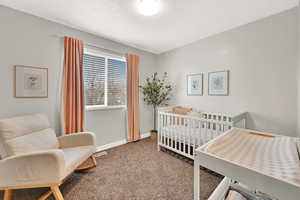 Carpeted bedroom with a textured ceiling and a crib