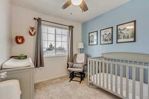 Bedroom featuring a nursery area, ceiling fan, and light colored carpet