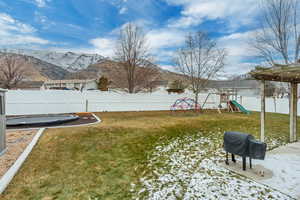 Yard covered in snow featuring a trampoline, a mountain view, and a playground