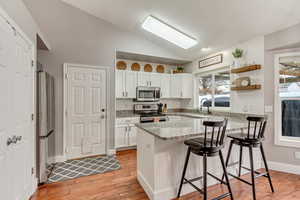 Kitchen with appliances with stainless steel finishes, white cabinetry, a kitchen breakfast bar, light stone counters, and vaulted ceiling