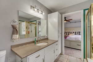 Bathroom featuring tile patterned floors, toilet, vanity, a shower with door, and ceiling fan