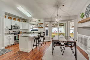 Kitchen with white cabinetry, appliances with stainless steel finishes, a center island, and vaulted ceiling