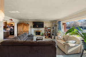 Living room with carpet floors, a textured ceiling, ornamental molding, and a stone fireplace