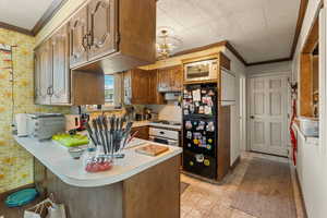 Kitchen with kitchen peninsula, a notable chandelier, black fridge, crown molding, and white gas cooktop