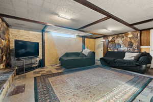 Living room with a textured ceiling, beam ceiling, and wood walls