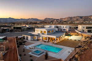 Back house at dusk featuring an in ground hot tub, a mountain view, and a patio