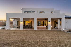 Back house at dusk featuring a yard, a patio area, outdoor lounge area, and ceiling fan