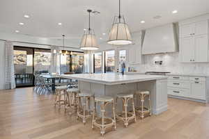 Kitchen featuring decorative light fixtures, custom exhaust hood, and a large island with sink